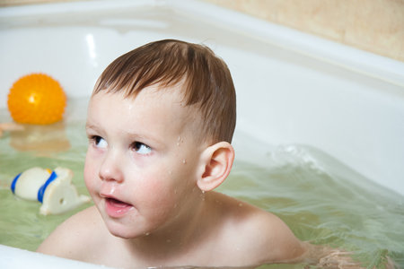 Happy child, little girl, bathes in a bubble bath, washes her face. The concept of childrens hygiene, joy, splashes, laughter, have fun. Family lifestyle.の写真素材