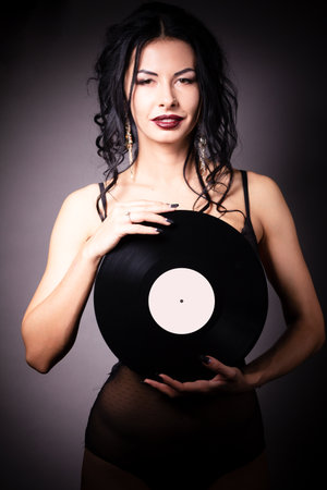 Vintage photo of a glamorous pinup girl, holding a vinyl record and looking up on a pink background.の写真素材