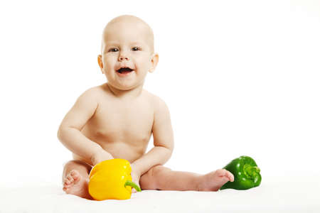 Cute healthy little girl in a pink bodysuit sitting with vegetables on a white background, isolate, the concept of the first lureの写真素材