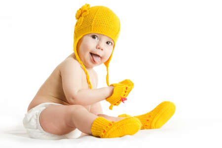 Little baby in knit winter clothing closing face with knitted beanie on the bed in the blue bedroom,...