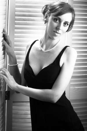 Gorgeous retro brunette woman with long hair in a little black dress and high heels walks on a white background. Beauty, sexuality, fashionable clothes. Full size, copy spaceの写真素材