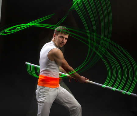 Light trail. Shooting with combined lighting. Young professional athlete plays with lighting equipment on a black background in mixed light. Working out in motion, action. Strength and energy.の写真素材