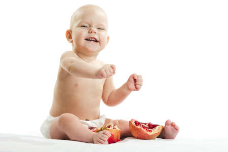 Laughing cute blonde child, girl sits and eats a pomegranate. Closeup portrait on isolated on white background.の写真素材