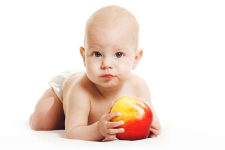 Happy child baby boy sitting in diaper and eating red yellow apple blue eyes looking at the corner isolated on a white backgroundの写真素材