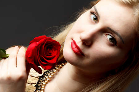 Beautiful happy girl holds red rose close to face and looks at camera.の写真素材