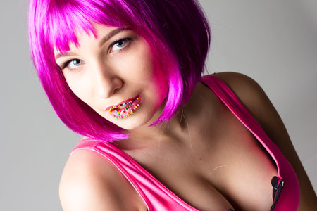 Face of a young woman with bright makeup on a pink background with gathered hair in a smooth ponytail.の写真素材