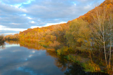 Sunrise in autumn by the lake, lake in the backlight of the rising sun, park in autumn and autumn leave in the sunlight in the morning, colorful leaves on the water, trees in the autumn by the waterの写真素材