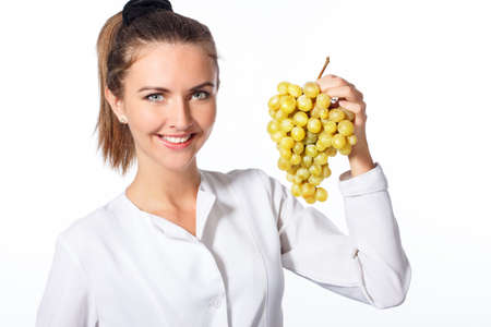 young attractive woman, holding a grape in one hand and a red apple in the other, looking joyful and happy, standing over isolated white background.の写真素材
