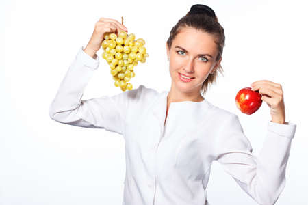 young attractive woman, holding a grape in one hand and a red apple in the other, looking joyful and happy, standing over isolated white background.の写真素材