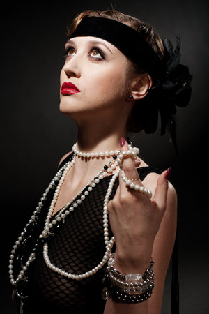 Portrait of a glamorous dark haired model with perfect makeup wearing a luxurious necklace, black bodysuit and long top, holding her hands behind her head and looking straight ahead.の写真素材