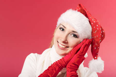 Beautiful young woman in santa claus hat and mittens smiling. Christmas tale. Red background. Postcard. Space for text.の写真素材