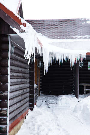 The house from logs with the iced over roof and hanging down icicles.の写真素材