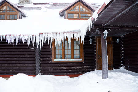 The house from logs with the iced over roof and hanging down icicles.の写真素材