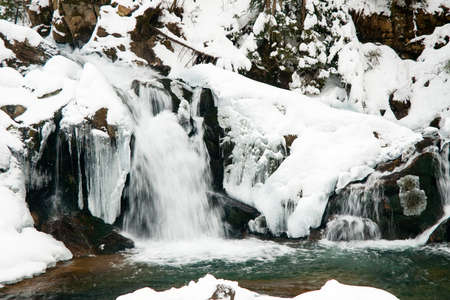 A small active waterfall. Clean mountain stream, snowy winter landscape, wildlife backgroundの写真素材