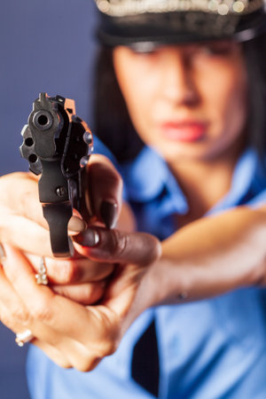 A girl in a uniform with a gun poses in the studio. The emphasis is on the gun, which is in the foreground.の写真素材