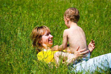 Young mother and her one year old daughter resting in the park on the grass. Family having fun together.の写真素材