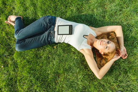 Close up portrait of an attractive young woman laying down on green grass in a park during the...