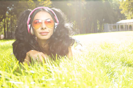 Horizontal portrait of pretty student girl spending day in park and showing thumb up. Cheerful young female enjoying time in country. Weekend and holiday conceptの写真素材