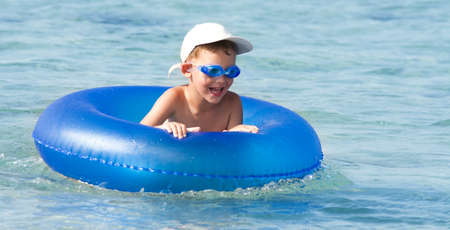 Happy boy with blond hair smiling sitting in swimming poolの写真素材