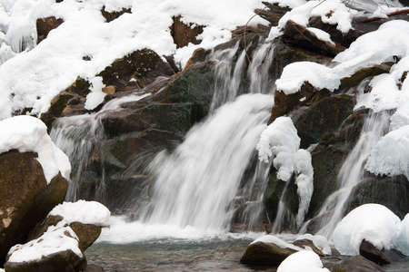 A small active waterfall. Clean mountain stream, snowy winter landscape, wildlife backgroundの写真素材