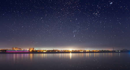 Abstract cityscape with modern high rise buildings skyscrapers and city lights reflected in mirror water surface of calm river or lake at dark night. With no people.の写真素材