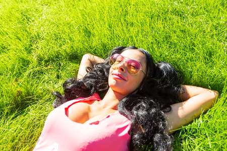 Horizontal portrait of pretty student girl spending day in park and showing thumb up. Cheerful young female enjoying time in country. Weekend and holiday conceptの写真素材