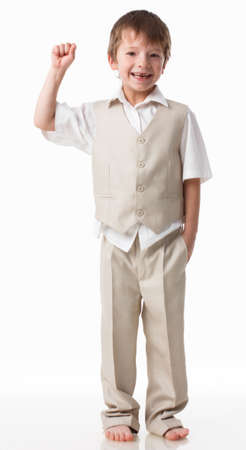 A handsome little boy dressed as a schoolboy - in a white shirt and gray trousers, stands against a white wall and poses, jumps like a model. isolated on white background.の写真素材