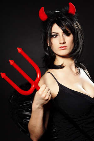 A beautiful, sexy woman in a devil costume, a demon with horns and pitchforks, a trident, in a red dress. American, dress for a costume party Halloween. Choker on the neck. Bright makeupの写真素材