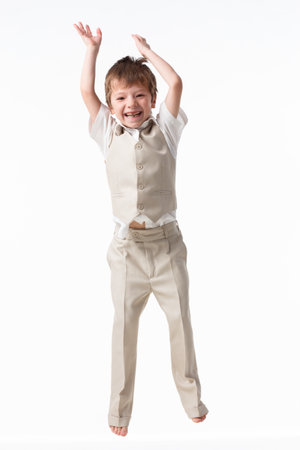 A handsome little boy dressed as a schoolboy - in a white shirt and gray trousers, stands against a white wall and poses, jumps like a model. isolated on white background.の写真素材