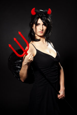 A beautiful, sexy woman in a devil costume, a demon with horns and pitchforks, a trident, in a red dress. American, dress for a costume party Halloween. Choker on the neck. Bright makeupの写真素材