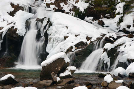 A small active waterfall. Clean mountain stream, snowy winter landscape, wildlife backgroundの写真素材