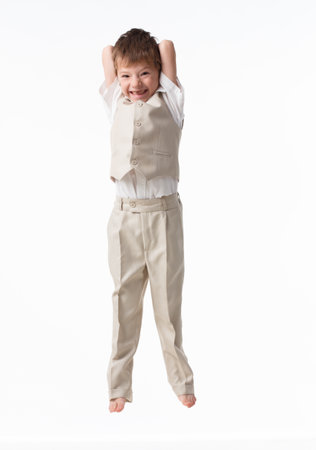 A handsome little boy dressed as a schoolboy - in a white shirt and gray trousers, stands against a white wall and poses, jumps like a model. isolated on white background.の写真素材
