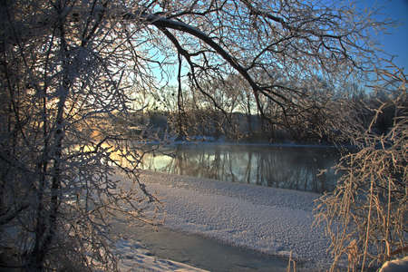 Photo the snow-covered river did not freeze in winter.The river flows in winter. Snow on the branches of trees. Reflection of snow in the river. Huge snowdrifts lie on the Bank of the stream.の写真素材