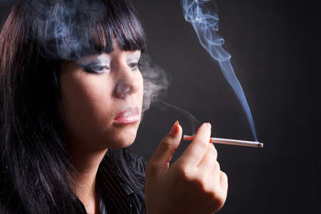 Smoking woman with cigarette smoke on black backgroundの写真素材