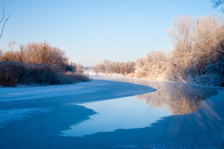 Photo the snow-covered river did not freeze in winter.The river flows in winter. Snow on the branches of trees. Reflection of snow in the river. Huge snowdrifts lie on the Bank of the stream.の写真素材