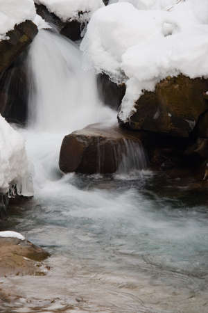 A small active waterfall. Clean mountain stream, snowy winter landscape, wildlife backgroundの写真素材