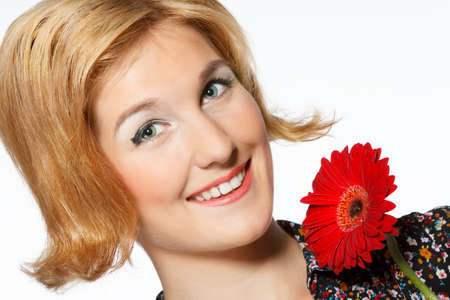A smiling beautiful young woman in a white dress with a bright red flower near her faceの写真素材