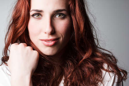 Beautiful red-haired cute girl with curly hair looking at the camera and smiling. The girl with a gentle makeup on her face. Freckles on the face of the girl.Joy, fun, positive, smiling girl.の写真素材