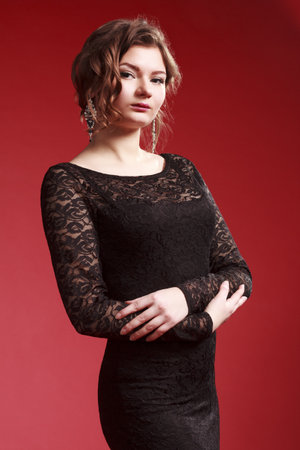 Beautiful girl in a black dress. Woman singer on a red background holds a golden microphone in her hands. Sings a songの写真素材