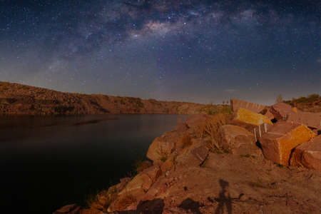 Milky Way over a lake in a granite quarry at night. Summer landscape with huge boulders, trees, purple sky with milky way and stars, beautiful reflection in the water. Ukraine. Space and nature.の写真素材