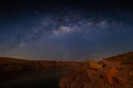 Milky Way over a lake in a granite quarry at night. Summer landscape with huge boulders, trees, purple sky with milky way and stars, beautiful reflection in the water. Ukraine. Space and nature.の写真素材