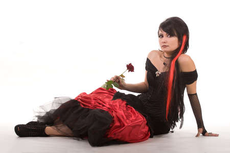 Beautiful young girl with red hair, wearing a long gothic black and red flamenco lace gown with black corset. kneeling on the ground. isolated on white background.の写真素材