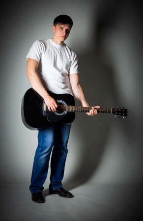 Full length portrait of handsome young man standing with guitar in room.の写真素材