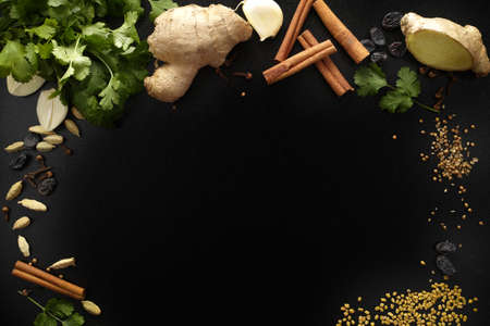 Indian spices, fresh coriander, ginger, garlic and dried cardamom, cloves, cinnamon, fenugreek on black background, copy spaceの写真素材