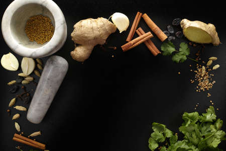 Marble mortar and indian spices, fresh coriander, ginger, garlic and dried cardamom, cloves, cinnamon on black background, copy spaceの写真素材