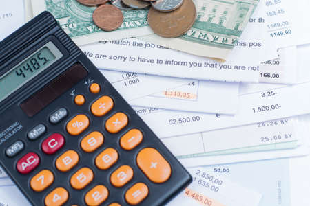 Mortgage and utility bills, foreign coins and dollars banknotes, calculator, different amountsの写真素材
