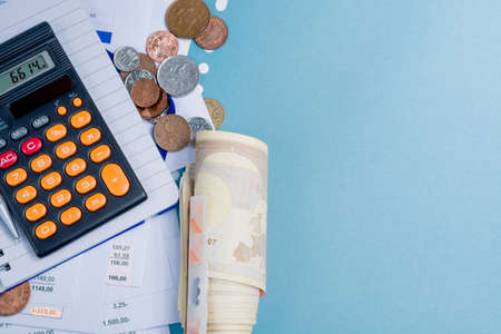 Mortgage and utility bills, foreign coins and roll of euro  banknotes, calculator, different amounts, on blue backgroundの写真素材