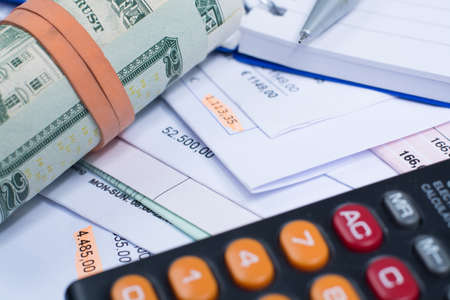 Invoices and bills, roll of dollars banknotes, calculator, different amounts, closeupの写真素材