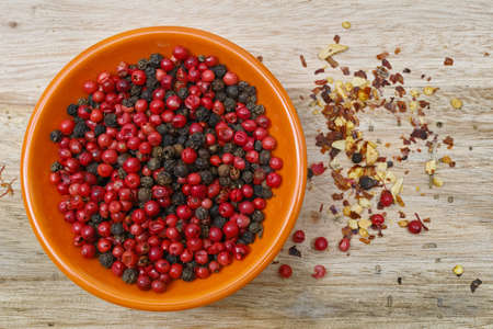 Red and black pepper in orange bowl on teak wood table top, closeupの写真素材
