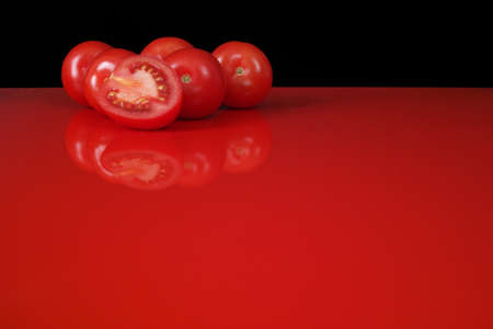 Fresh red Roma tomatoes on red table  top with reflection and black background, copy spaceの写真素材
